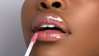 Close-up of a person's lips being applied with a pink lip gloss using a wand applicator.