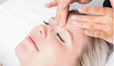 Calm facial treatment at Yazdani Aesthetics: a client with closed eyes receives a close-up forehead massage under bright light, showcasing relaxation and spa care with a clean white towel backdrop.