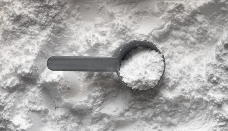 A dark measuring scoop rests in a mound of white collagen powder on a pale surface, echoing the discussion of supplements and skin health.