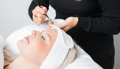 Client with a white headband receives a facial treatment as a clinician applies product with a brush, referencing Cleopatra and the Ebers Papyrus in skincare history.