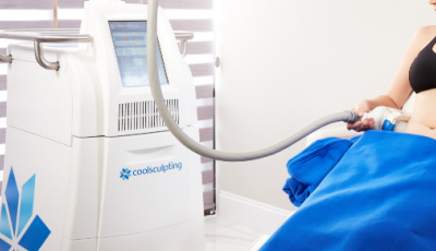 A patient receives CoolSculpting treatment with a cooling applicator connected to a body contouring device in a bright Yazdani Aesthetics clinic room.