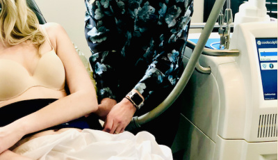 Medical procedure scene with a patient partially dressed, using a CoolSculpting device in a clinical setting, featuring a blue-toned staff member and modern equipment.