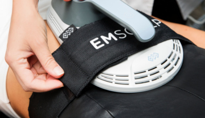 EMSCULPT device being applied to a person's lower back with a black strap securing it in place.