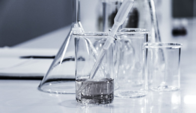 Glass laboratory equipment including a graduated cylinder, pipette, and beakers on a work surface.