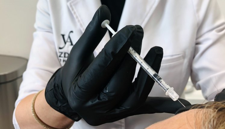A gloved hand holding a syringe, preparing for an injection in a clinical setting.